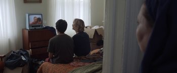 Movie still from “After Love” (2020), directed by Aleem Khan – A couple of people sitting on top of a bed next to a window; Medium shot, Over the shoulder angle