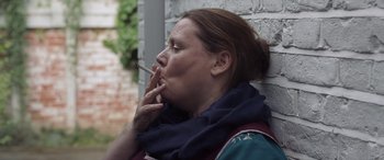 Movie still from “After Love” (2020), directed by Aleem Khan – A woman is smoking a cigarette in front of a brick wall; Close Up shot, Over the shoulder angle