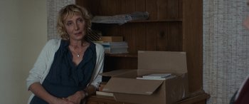 Movie still from “After Love” (2020), directed by Aleem Khan – A woman sitting in front of a box in a room; Medium shot, Over the shoulder angle