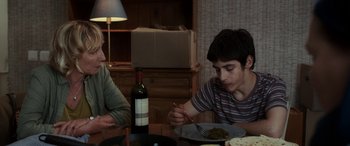 Movie still from “After Love” (2020), directed by Aleem Khan – Two people sitting at a table with a plate of food and a bottle of wine; Medium shot, Over the shoulder angle