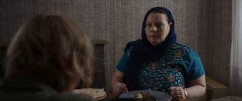 Movie still from “After Love” (2020), directed by Aleem Khan – An older woman sitting at a table with a plate of food in front of her; Medium shot, Over the shoulder angle