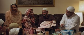 Movie still from “After Love” (2020), directed by Aleem Khan – A man and a woman sitting on a couch holding a baby; Medium shot, Over the shoulder angle