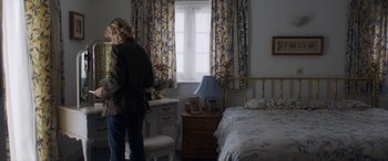 Movie still from “After Love” (2020), directed by Aleem Khan – A woman standing in front of a bed in a bedroom; Medium shot, High angle