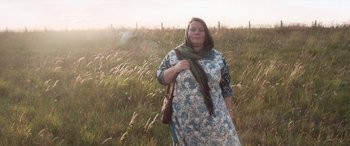 Movie still from “After Love” (2020), directed by Aleem Khan – A woman standing in a grassy field holding a purse; Medium shot, Low angle