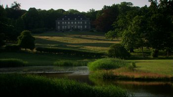 Movie still from “After the Wedding” (2006), directed by Susanne Bier – A house in the middle of a field with a body of water in front of it; Extreme Wide shot, Low angle