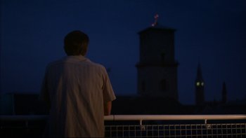Movie still from “After the Wedding” (2006), directed by Susanne Bier – A man standing on a balcony looking at a clock tower at night; Wide shot, Low angle