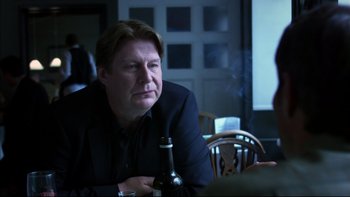 Movie still from “After the Wedding” (2006), directed by Susanne Bier – A man sitting at a table with a bottle of wine; Close Up shot, Over the shoulder angle