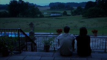 Movie still from “After the Wedding” (2006), directed by Susanne Bier – A man and a woman sitting on a porch looking out over a field; Wide shot, High angle