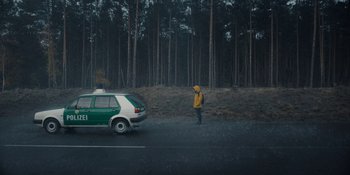 Movie still from “Dark” (2017), created by Baran bo Odar – A man standing on the side of a road next to a car; Wide shot, Low angle