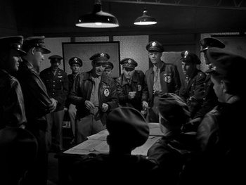 Movie still from “Air Force” (1943), directed by Howard Hawks – Black and white photograph of a group of men standing around a table; Medium shot, High angle