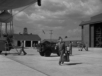 Movie still from “Air Force” (1943), directed by Howard Hawks – An old photo of a man walking in front of an army vehicle; Extreme Wide shot, Low angle