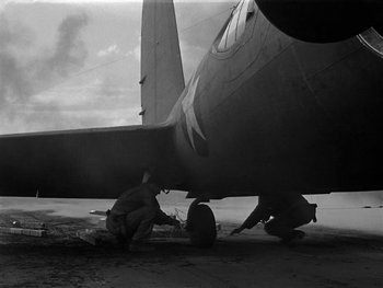 Movie still from “Air Force” (1943), directed by Howard Hawks – A man working on the underside of an airplane; Wide shot, Low angle