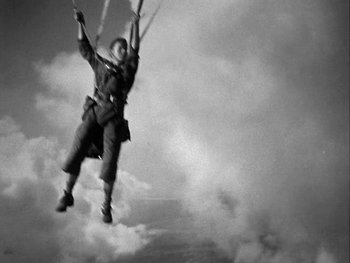 Movie still from “Air Force” (1943), directed by Howard Hawks – A man in the air holding onto a parachute; Wide shot, Low angle