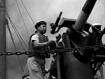 Movie still from “Air Force” (1943), directed by Howard Hawks – An old photo of a man working on a machine; Medium shot, Low angle