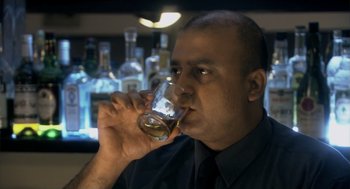 A man in a black shirt drinking a glass of whiskey