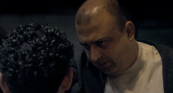 A man with a shaved head is looking at another man with curly hair