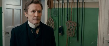 Movie still from “Albert Nobbs” (2011), directed by Rodrigo García – A man wearing a suit and tie standing in a room; Close Up shot, Over the shoulder angle