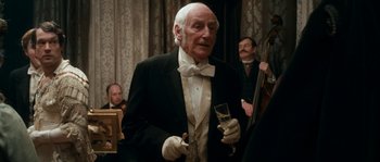 Movie still from “Albert Nobbs” (2011), directed by Rodrigo García – An old man in a tuxedo holding a glass of wine; Medium shot, Over the shoulder angle