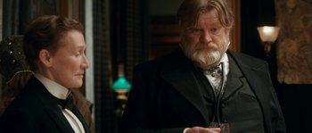 Movie still from “Albert Nobbs” (2011), directed by Rodrigo García – An old man with a beard and mustache wearing a black suit and holding a wine glass; Medium shot, Over the shoulder angle