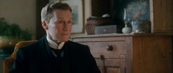 Movie still from “Albert Nobbs” (2011), directed by Rodrigo García – A man in a suit and tie sitting in front of a wooden dresser; Close Up shot, Over the shoulder angle