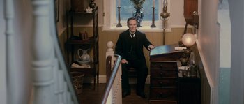 Movie still from “Albert Nobbs” (2011), directed by Rodrigo García – A man sitting on a chair in a room; Wide shot, High angle