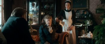Movie still from “Albert Nobbs” (2011), directed by Rodrigo García – An old woman sitting in a chair next to a woman in a maid's uniform; Medium shot, Over the shoulder angle