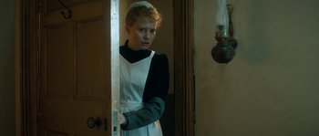 Movie still from “Albert Nobbs” (2011), directed by Rodrigo García – A woman in a maid's uniform standing in front of an open door; Medium shot, High angle