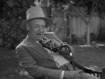 Movie still from “Alice Adams” (1935), directed by George Stevens – An older man sitting in a chair wearing a hat and holding a camera; Close Up shot, High angle