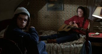 Movie still from “Alice's Restaurant” (1969), directed by Arthur Penn – A man and a woman sitting on a bed with a guitar; Medium shot, High angle