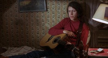 Movie still from “Alice's Restaurant” (1969), directed by Arthur Penn – A woman sitting on a bed holding a guitar; Medium shot, High angle