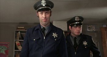 Movie still from “Alice's Restaurant” (1969), directed by Arthur Penn – Two men in police uniforms are posing for a picture; Medium shot, Low angle