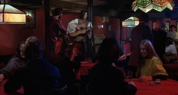 Movie still from “Alice's Restaurant” (1969), directed by Arthur Penn – A group of people sitting at a table with a guitar; Wide shot, Low angle