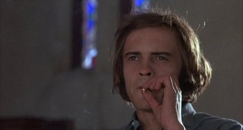 Movie still from “Alice's Restaurant” (1969), directed by Arthur Penn – A man smoking a cigarette in front of a stained glass window; Close Up shot, Low angle