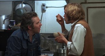 A man and a woman eating food in a kitchen