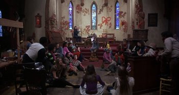 Movie still from “Alice's Restaurant” (1969), directed by Arthur Penn – A group of people sitting in a room with stained glass windows on the walls; Wide shot, High angle