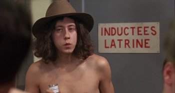 Movie still from “Alice's Restaurant” (1969), directed by Arthur Penn – A young man with a hat and a sign in the background; Medium shot, Low angle