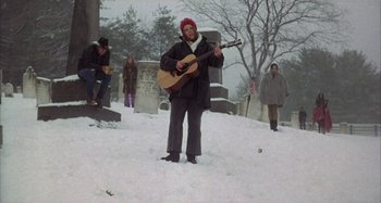 Movie still from “Alice's Restaurant” (1969), directed by Arthur Penn – A man playing a guitar in the middle of a snowy field; Wide shot, Low angle