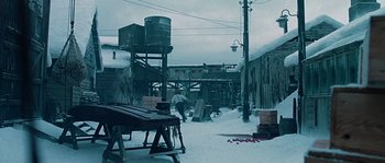 Movie still from “Alien vs. Predator” (2004), directed by Paul W.S. Anderson – A man standing next to a wooden table in the middle of a snow covered yard; Extreme Wide shot, High angle