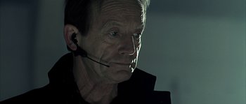 Movie still from “Alien vs. Predator” (2004), directed by Paul W.S. Anderson – An older man wearing a black jacket and a headset; Close Up shot, Low angle