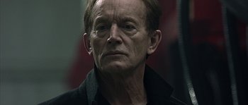 Movie still from “Alien vs. Predator” (2004), directed by Paul W.S. Anderson – An older man wearing glasses and a black shirt; Close Up shot, Low angle