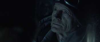 Movie still from “Alien vs. Predator” (2004), directed by Paul W.S. Anderson – An older man wearing goggles looking up at the sky; Close Up shot, Over the shoulder angle