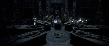 Movie still from “Alien vs. Predator” (2004), directed by Paul W.S. Anderson – A group of people standing in a room with many statues; Wide shot, High angle