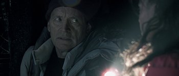 Movie still from “Alien vs. Predator” (2004), directed by Paul W.S. Anderson – An older man looking at the camera with a flashlight in his hand; Close Up shot, Over the shoulder angle
