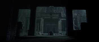 Movie still from “Alien vs. Predator” (2004), directed by Paul W.S. Anderson – A person sitting on the ground in front of a building; Extreme Wide shot, Low angle