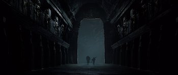 Movie still from “Alien vs. Predator” (2004), directed by Paul W.S. Anderson – Two people are walking through an archway in the dark; Extreme Wide shot, Low angle