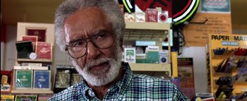 Movie still from “All About the Benjamins” (2002), directed by Kevin Bray – An older man wearing glasses and a plaid shirt in a store; Close Up shot, Over the shoulder angle