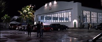 Movie still from “All About the Benjamins” (2002), directed by Kevin Bray – Two people standing in a parking lot next to a building; Extreme Wide shot, Low angle