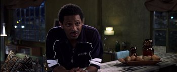 Movie still from “All About the Benjamins” (2002), directed by Kevin Bray – A man sitting at a table in front of a lamp; Close Up shot, Over the shoulder angle