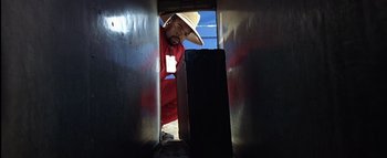 Movie still from “All About the Benjamins” (2002), directed by Kevin Bray – A man in a red suit and hat looking into an open door; Medium shot, Low angle