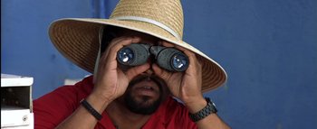 Movie still from “All About the Benjamins” (2002), directed by Kevin Bray – A man wearing a straw hat looking through binoculars; Extreme Close Up shot, High angle